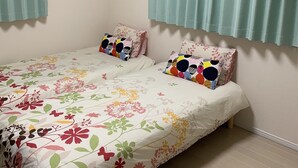 A bedroom with a bed, two pillows, a window with curtains, and an air conditioning unit on the wall. - Nara Guesthouse Kaede (Nara)