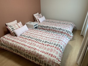A bedroom with two beds, each with patterned bedding, a bedside table, and a nightstand.
