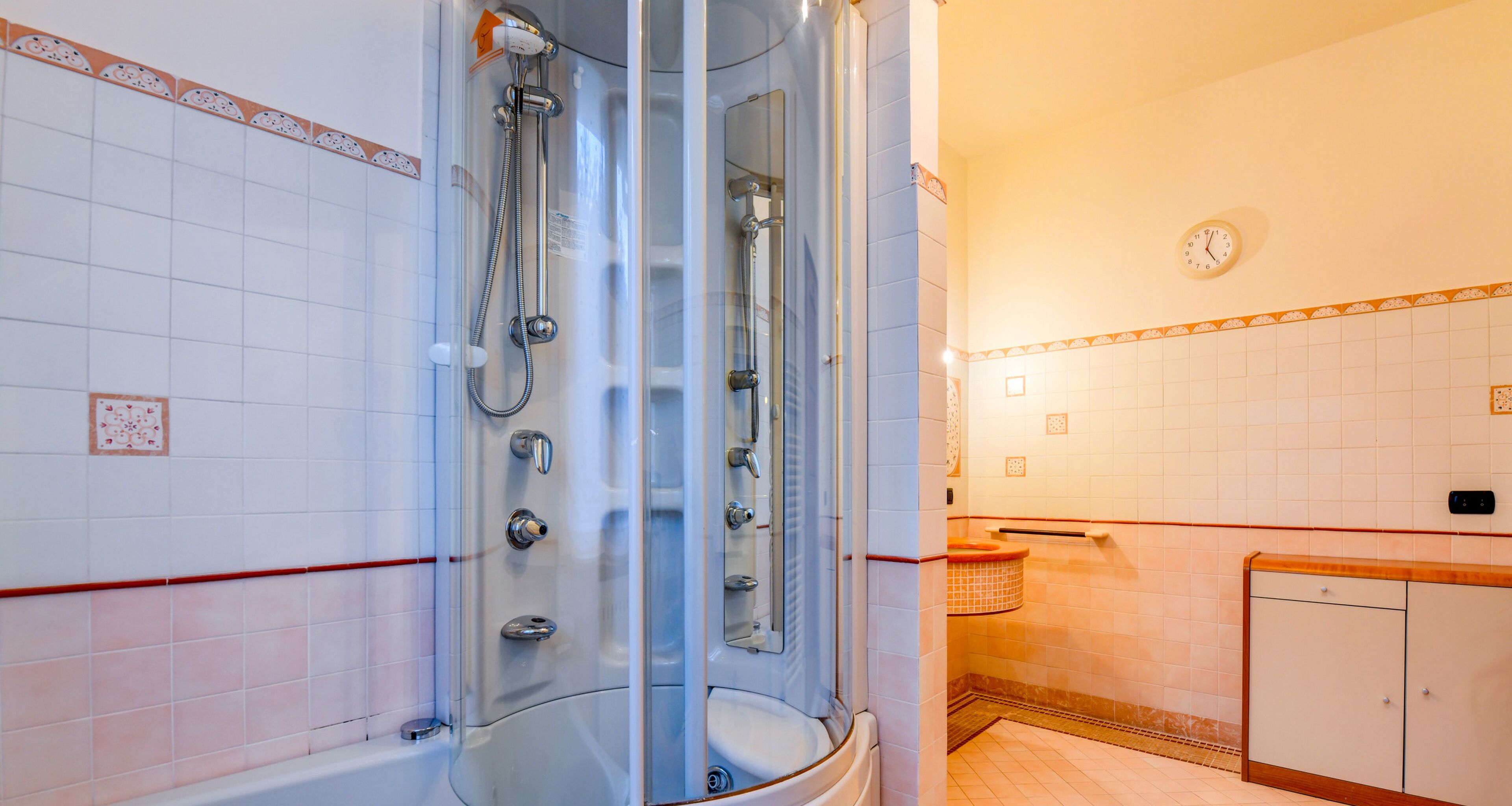 A bathroom with a glass-enclosed shower, a white sink, and a clock on the wall.