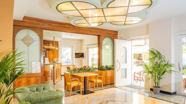 A spacious lobby with a marble floor, a green sofa, a wooden dining area, and a kitchen visible through an open door. - Hotel Centrale (Garda)