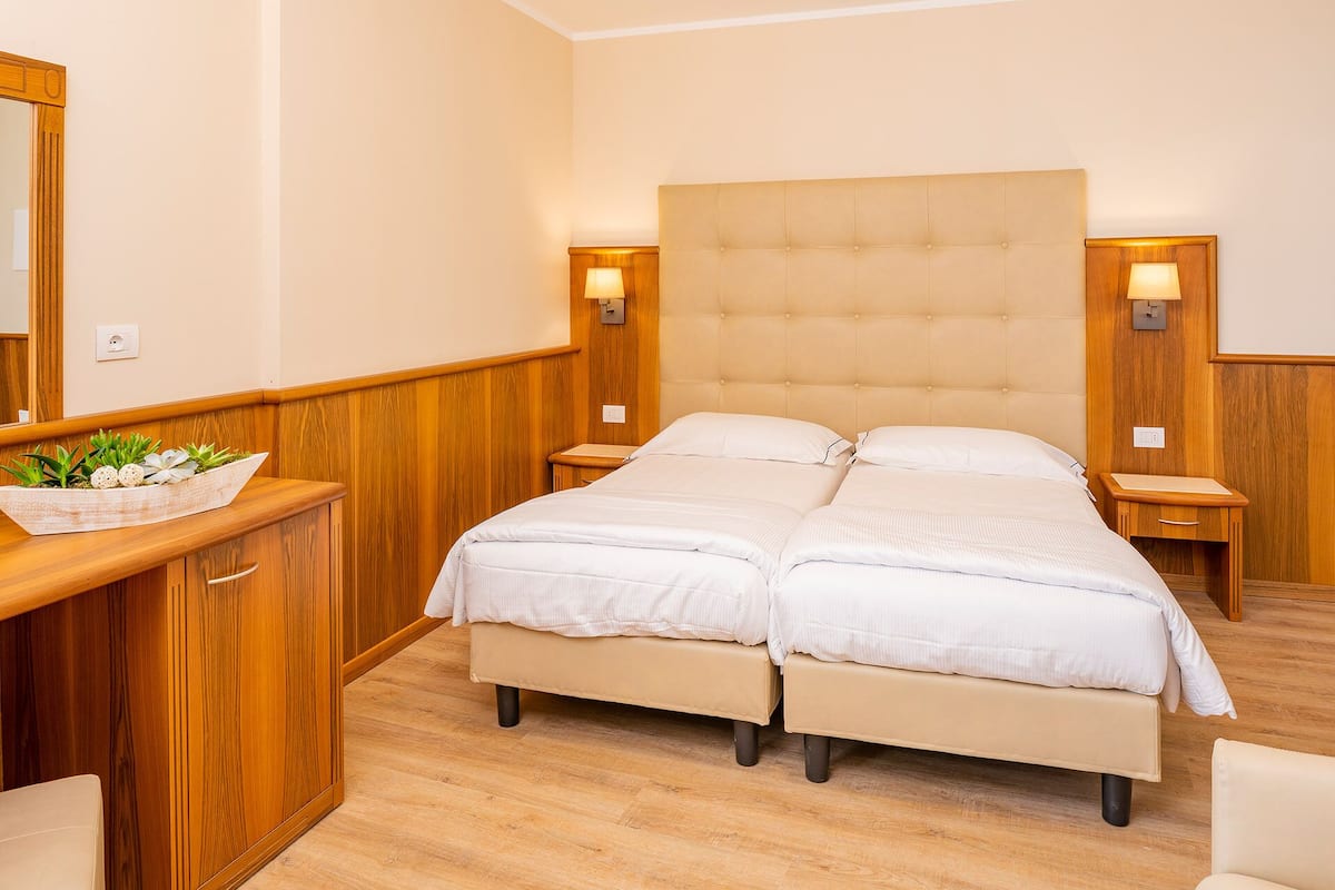 A double bed with a tufted headboard, wooden nightstands, a wooden dresser with a mirror, and a small plant on the dresser.