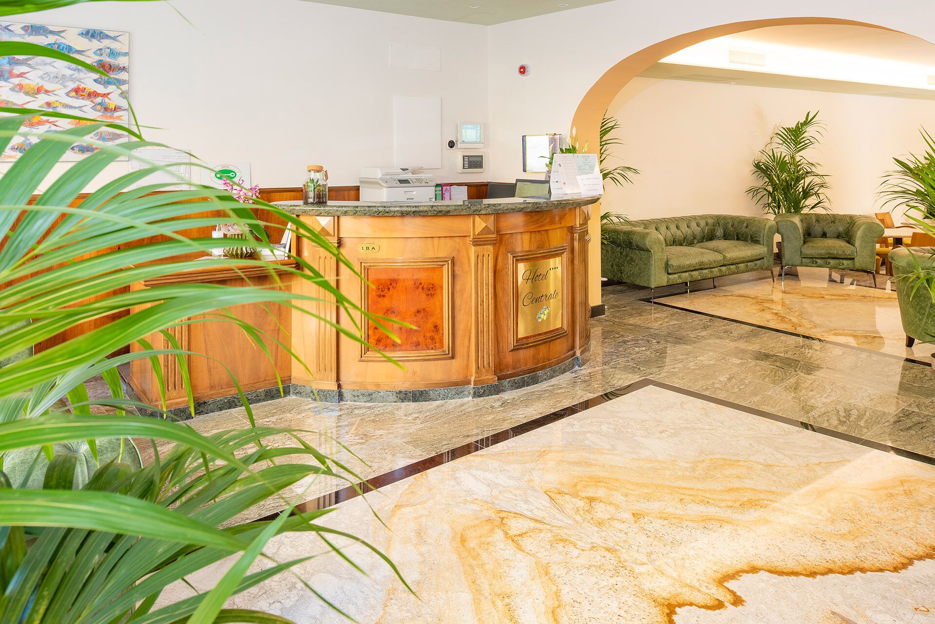 A hotel lobby with a reception desk, a green sofa, and a marble floor.