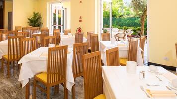 A dining area with multiple tables and chairs, a fire extinguisher, and a view of the garden.