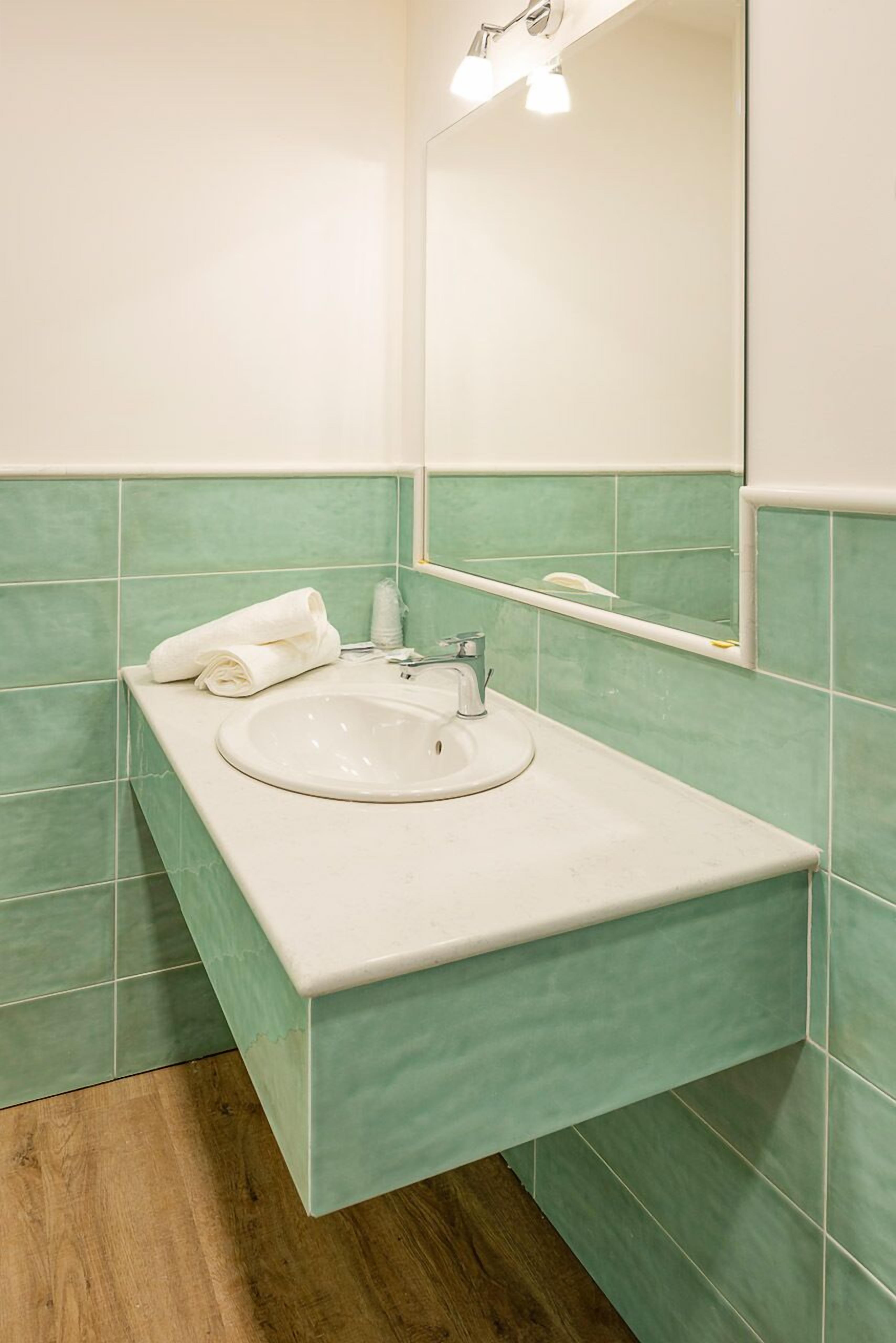 Une salle de bain avec un lavabo blanc, des carreaux verts, un miroir et une serviette posée sur le comptoir.
