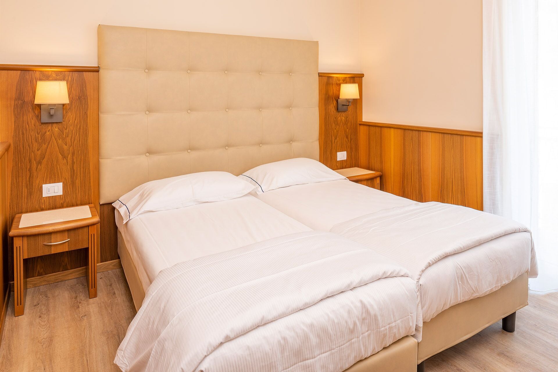 Ein Doppelbett mit einem gepolsterten Kopfteil, zwei Nachttische mit Lampen und eine Wandpaneele aus Holz.