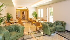 A spacious lobby with green leather sofas, a marble floor, and a dining area with wooden tables and chairs. - Hotel Centrale (Garda)
