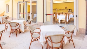 An outdoor dining area with wicker chairs and white tablecloths, connected to an indoor dining space by glass doors. - Hotel Centrale (Garda)