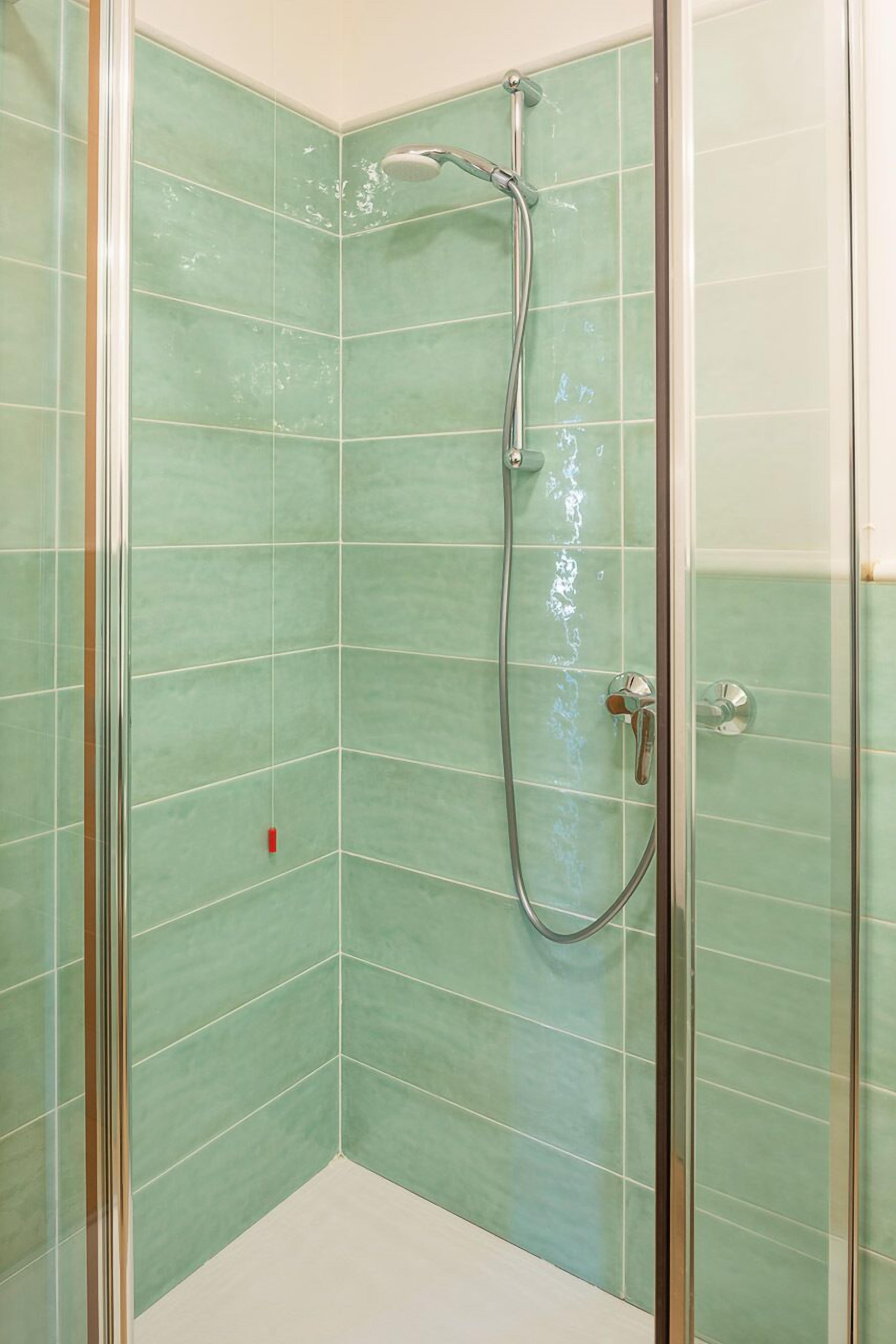 A glass-enclosed shower with a handheld showerhead and a wall-mounted faucet.