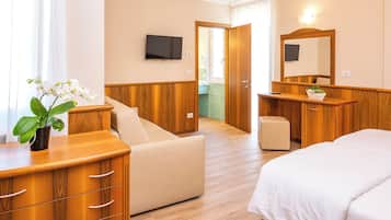 A hotel room with a bed, a wooden dresser, a small table, a chair, a TV, and a bathroom visible through an open door.