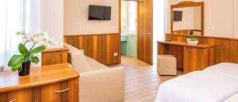 A hotel room with a bed, a wooden dresser, a small table, a chair, a TV, and a bathroom visible through an open door.