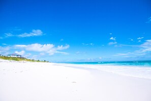 Ein Strand mit einem Haus links, blauem Himmel und türkisblauem Meer.