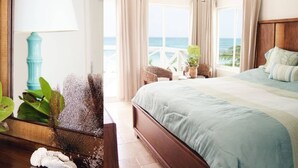 Une chambre d’hôtel avec un grand lit, une vue sur l’océan, un balcon doté de meubles en osier et une plante en pot.