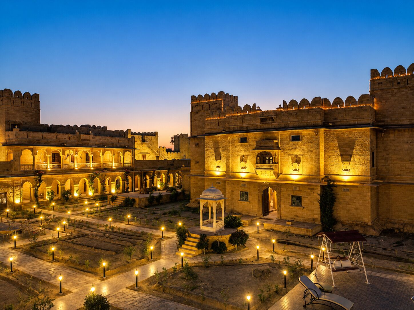 A historic building with a courtyard, illuminated by street lamps, and a swing set.