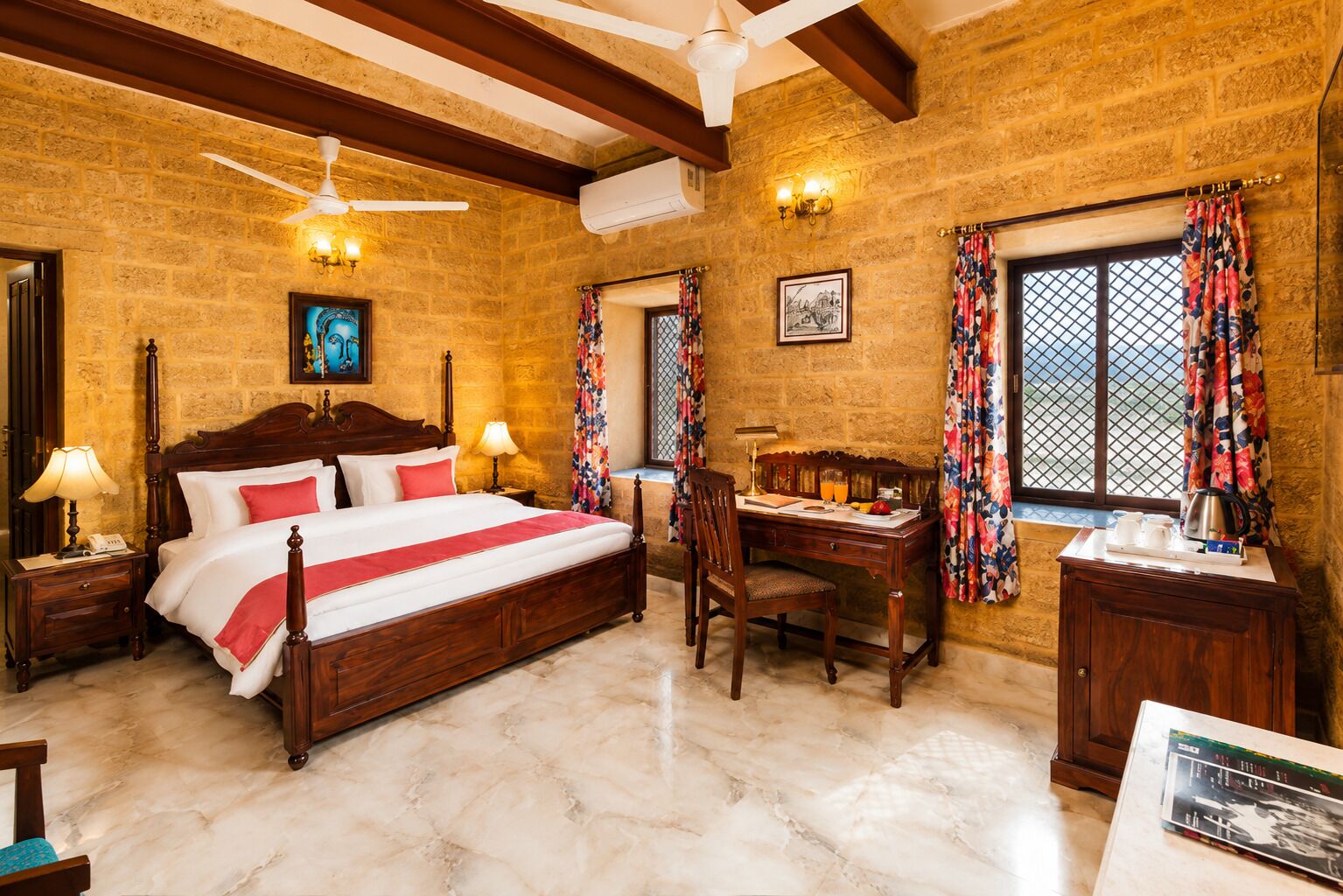 Une chambre d’hôtel avec un lit en bois, un bureau, une chaise, une fenêtre avec des rideaux, un ventilateur de plafond et un climatiseur fixé au mur.