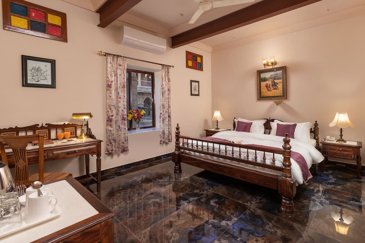 Quarto com cama de madeira, escrivaninha e cadeira. Há uma janela com cortinas e um quadro na parede.