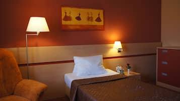 Comfortable retreat with a neatly made bed, a chair, and a nightstand with a lamp, plus a beautiful painting and a small table with a vase of flowers.