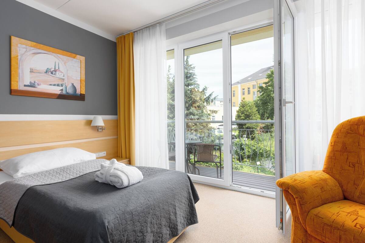 Une chambre d’hôtel avec un lit, une chaise, un tableau au mur et un balcon avec vue.