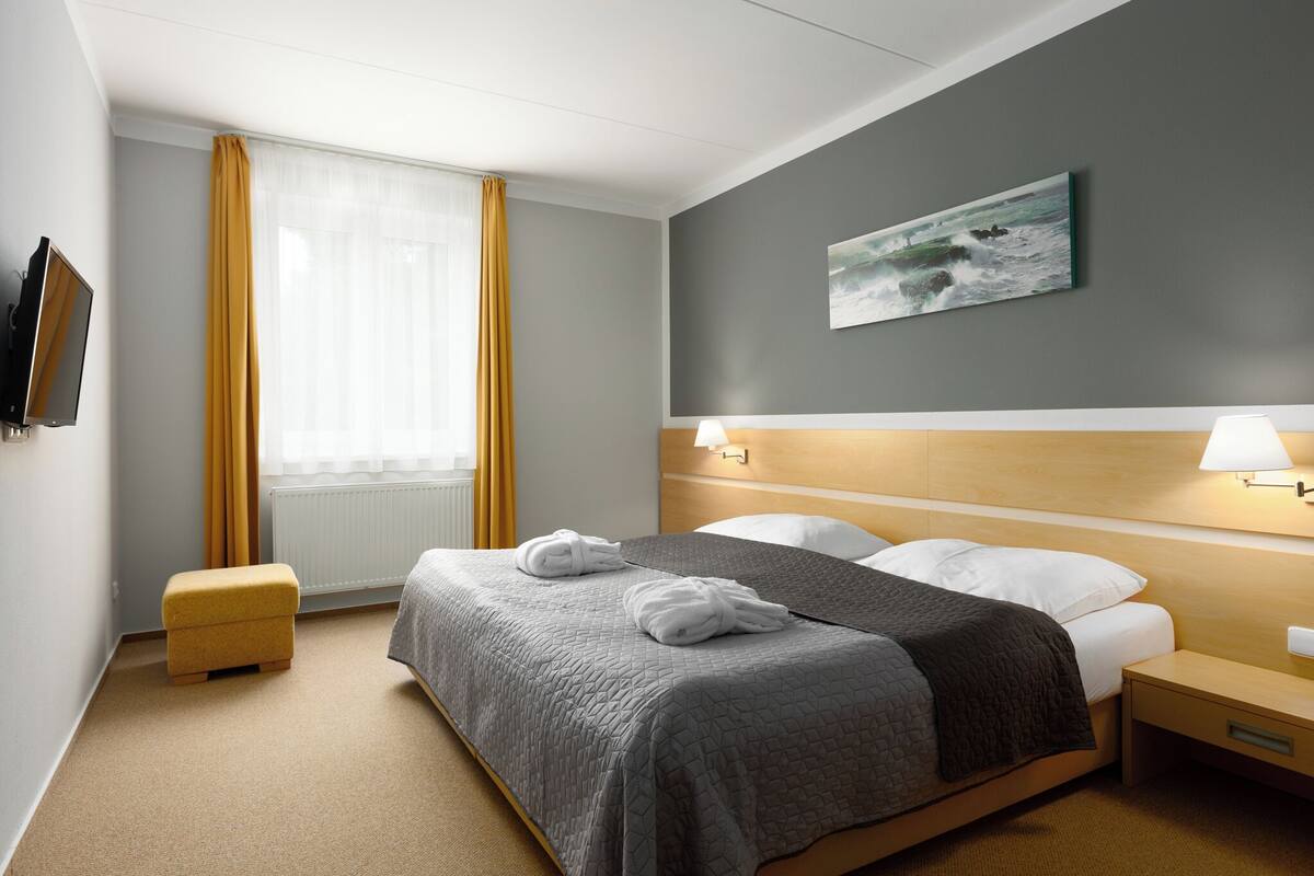 Une chambre d’hôtel avec un lit, des lampes de chevet, un tableau au mur et une fenêtre avec des rideaux.