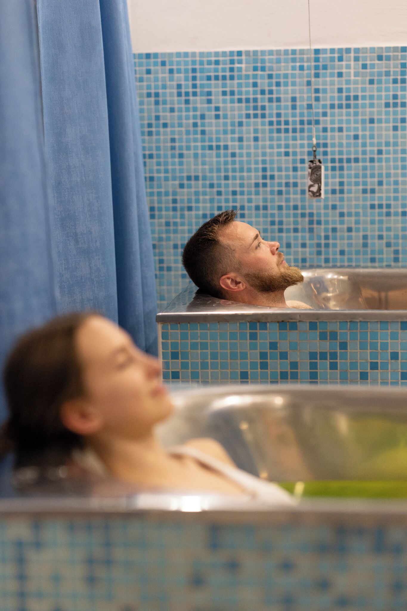 A person relaxing in a bathtub with a tiled wall behind them.