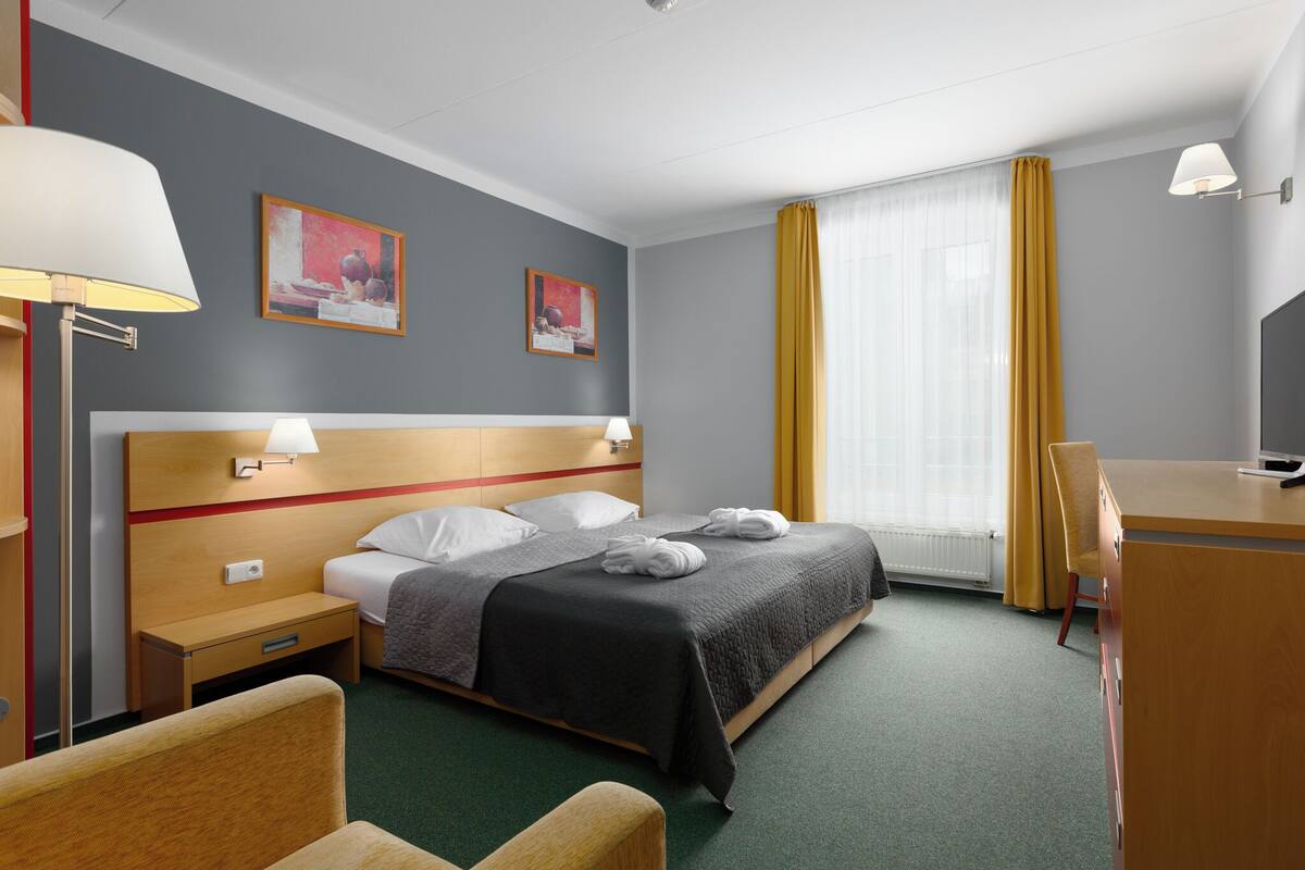 Une chambre d’hôtel avec un lit, des lampes de chevet, un bureau et une chaise.