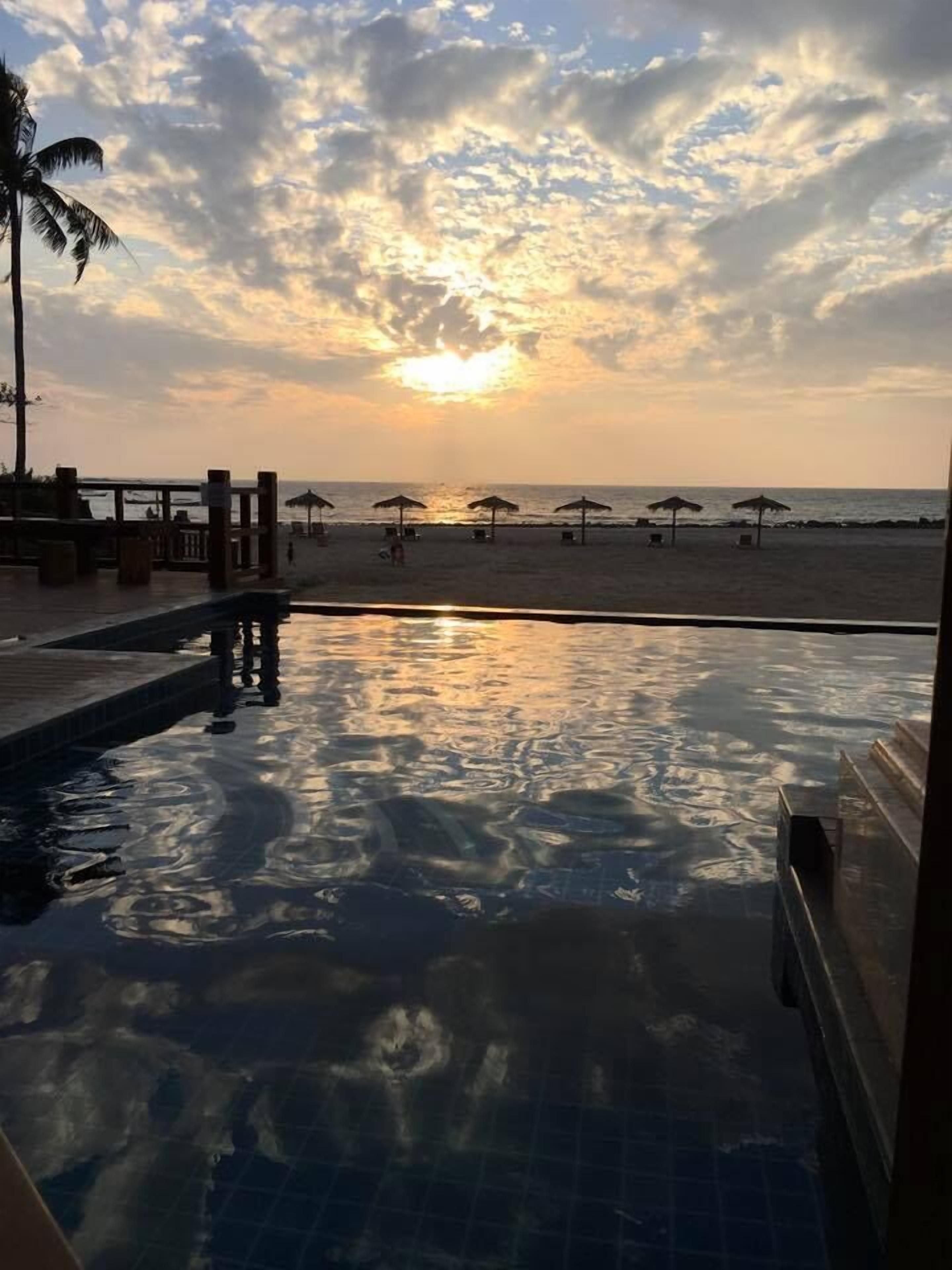 Une piscine offrant une vue sur la plage et l’océan au coucher du soleil.
