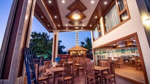 Un espace extérieur aménagé pour les repas, avec des tables et des chaises en bois, une structure centrale également en bois, et une vue sur le ciel.