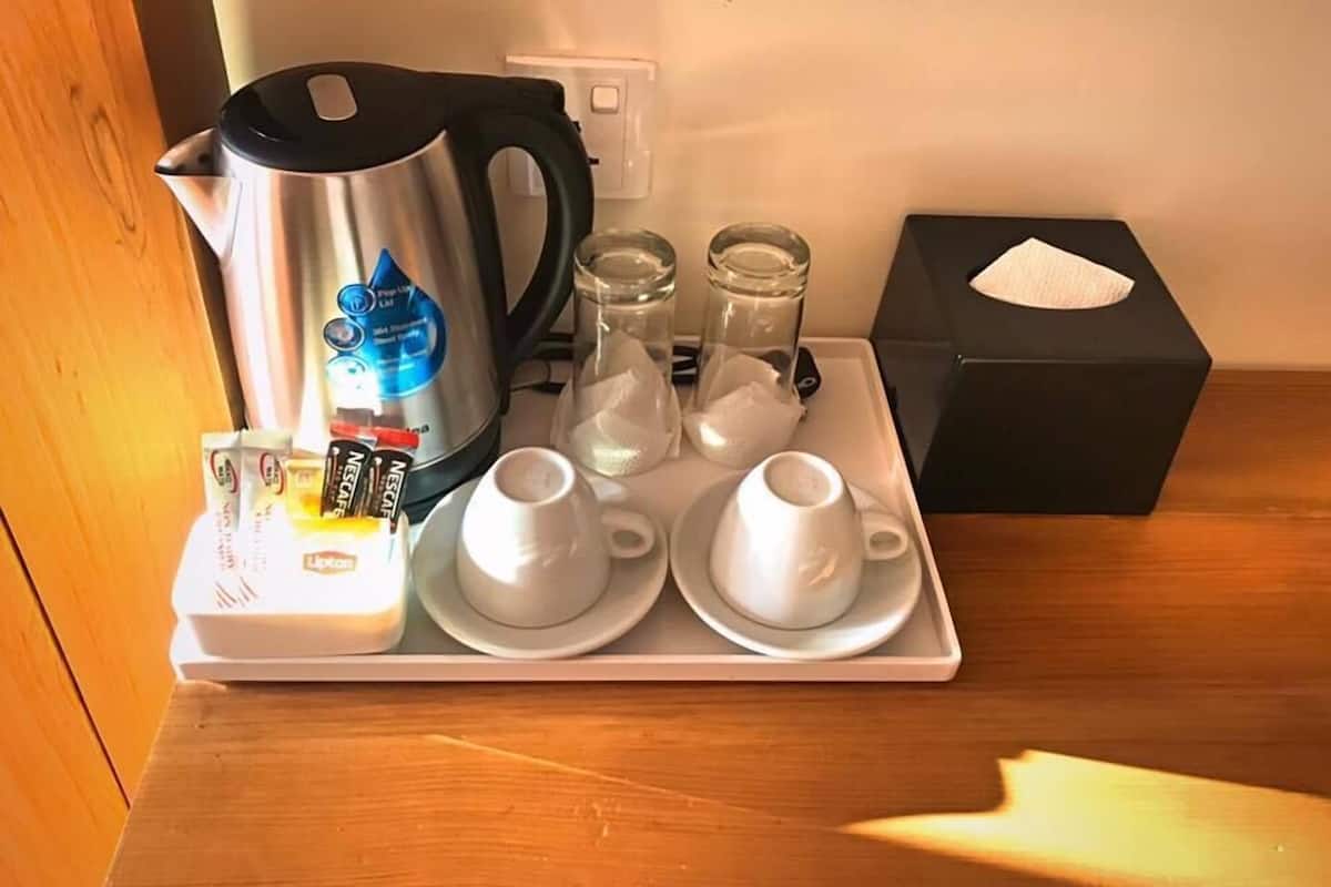 Una bandeja con cafetera, sobres de azúcar, leche condensada y dos tazas blancas sobre una mesa de madera.