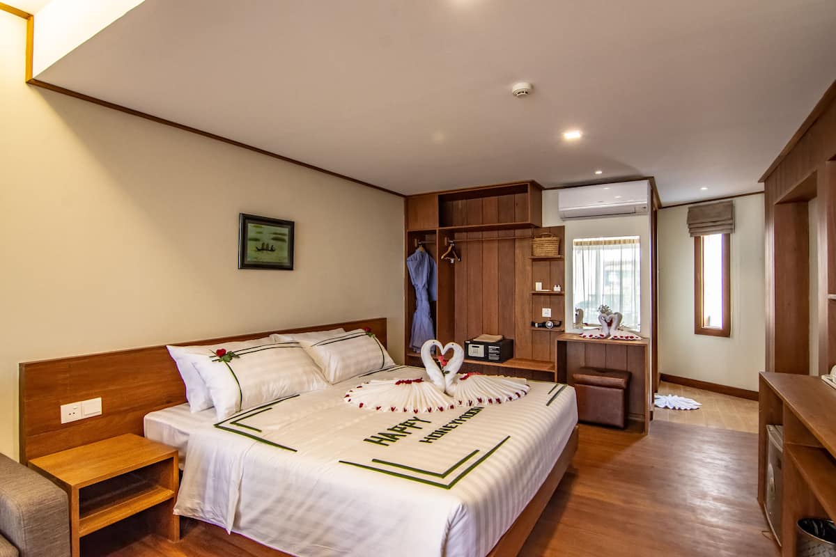 Una habitación de hotel con una cama grande, cabecera de madera, un escritorio pequeño y un armario.