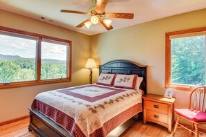 Ein Schlafzimmer mit Bett, Nachttisch, Sessel, Deckenventilator und großen Fenstern mit Blick ins Freie.