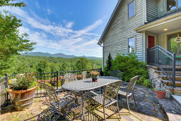 Eine Terrasse mit Tisch und Stühlen, einem Blumentopf und einem Steinweg, der zu einem Haus mit roter Tür und Treppe führt.