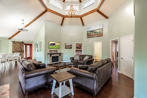 A spacious living room with leather sofas, a fireplace, and a dining area with white chairs.