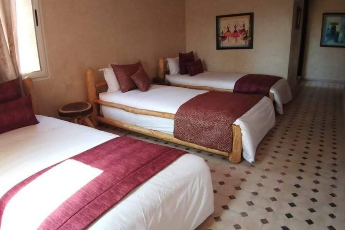 A room with three single beds, each with a wooden frame and white bedding, arranged in a row.