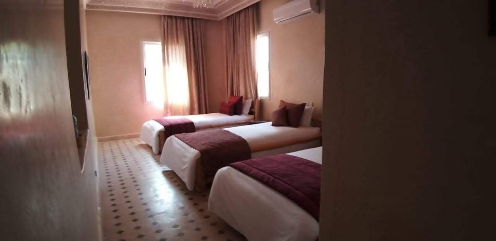 Quarto de hotel com duas camas, soalho estampado e janela com cortinas.