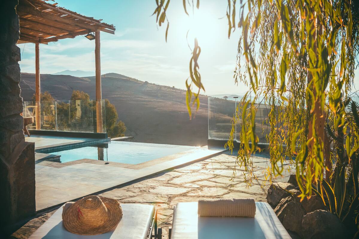 A poolside area with stone flooring, a pergola, and a view of distant hills.