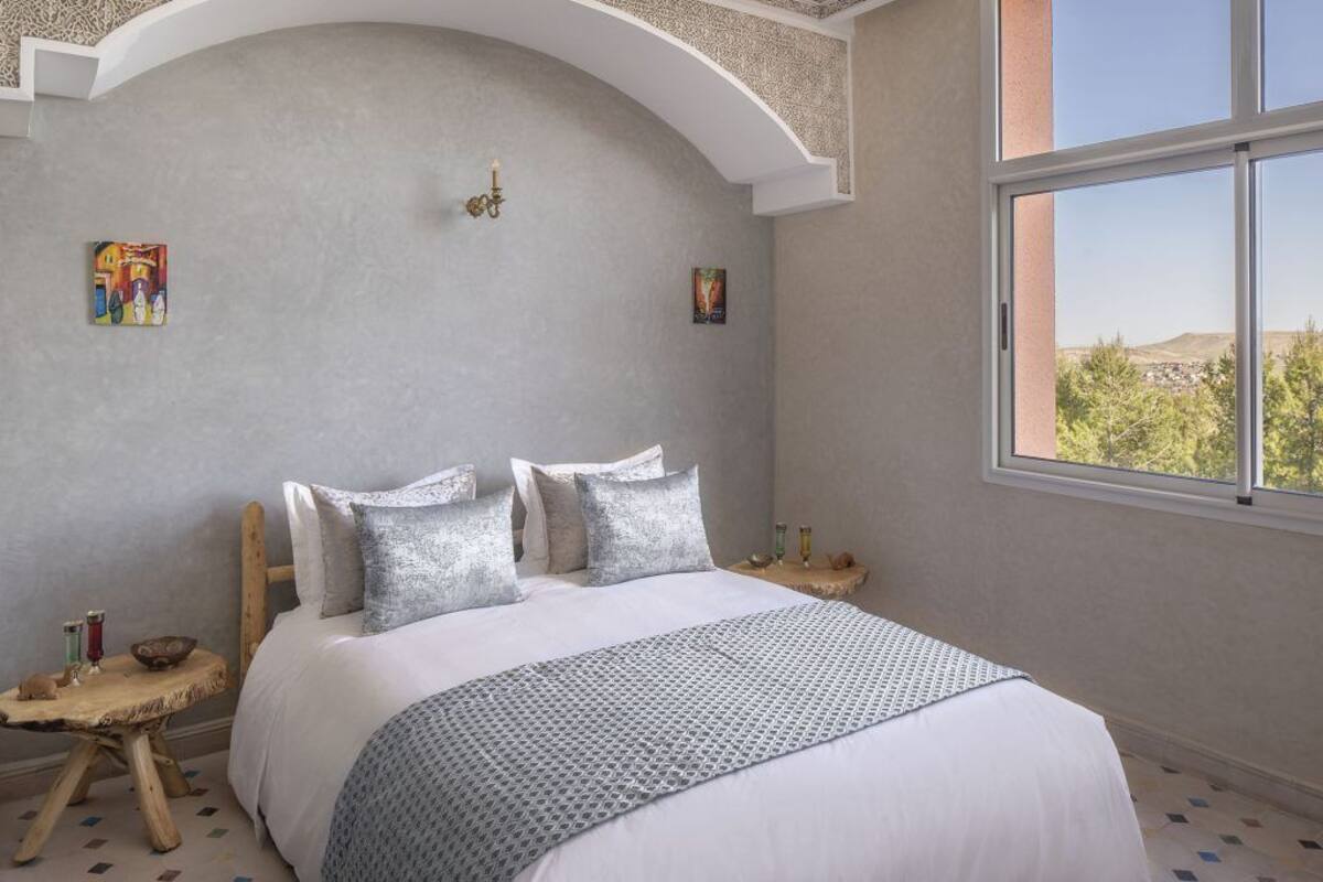 A bedroom with a large bed, a view of the outdoors, and a unique ceiling design.