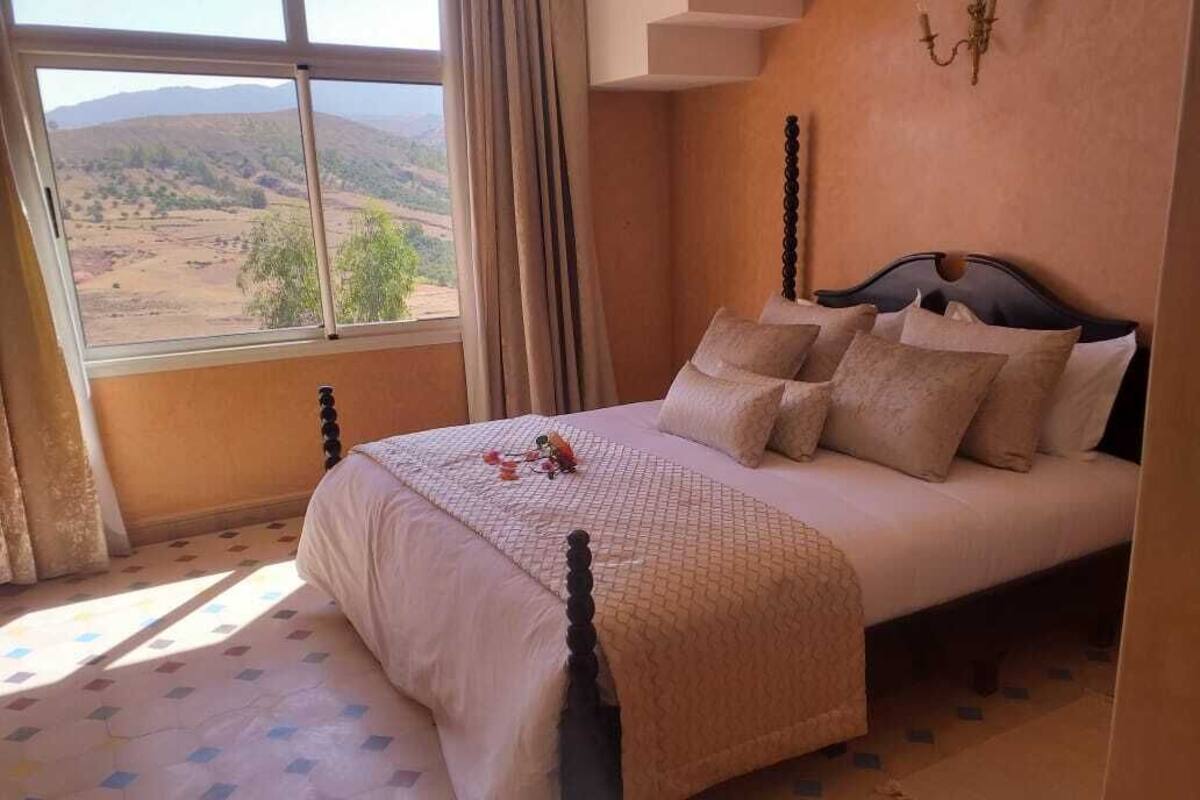 A bedroom with a bed, a window with a view of the countryside, and a chandelier on the wall.
