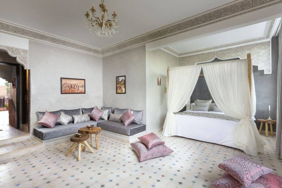A bedroom with a sofa, a bed with a canopy, a small table, and a patterned floor.