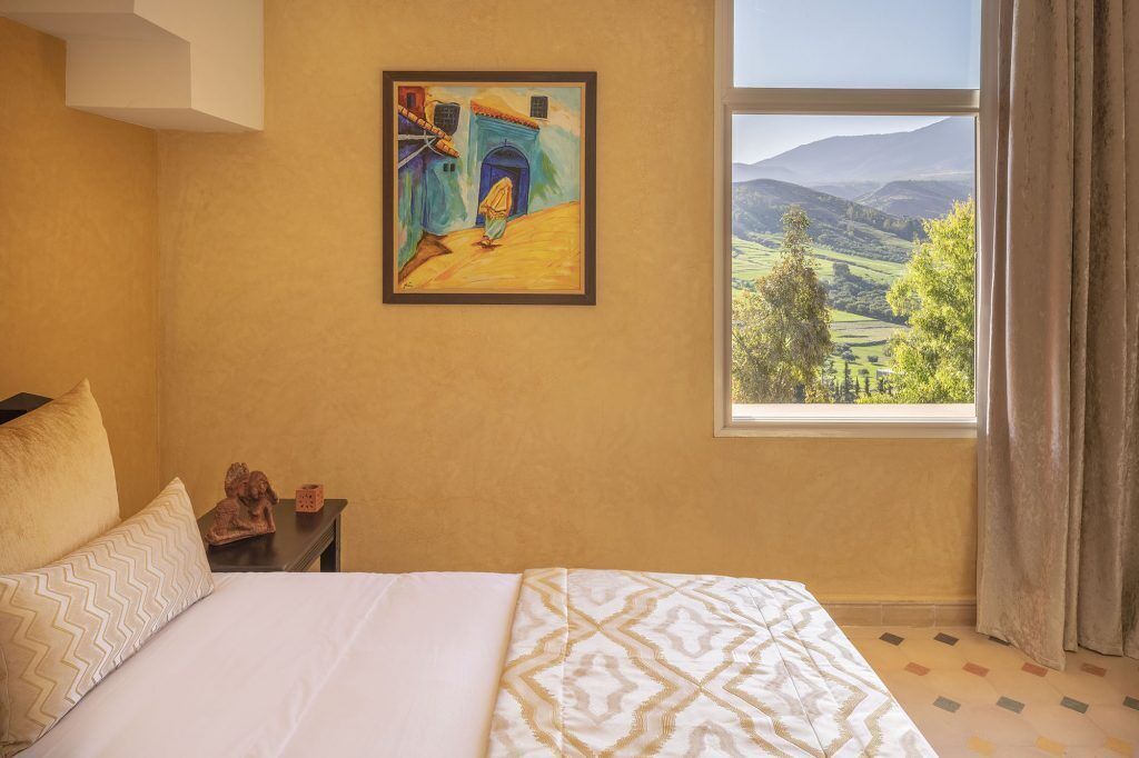 Un dormitorio con cama, un cuadro, una mesita de noche y una ventana con vistas al paisaje.