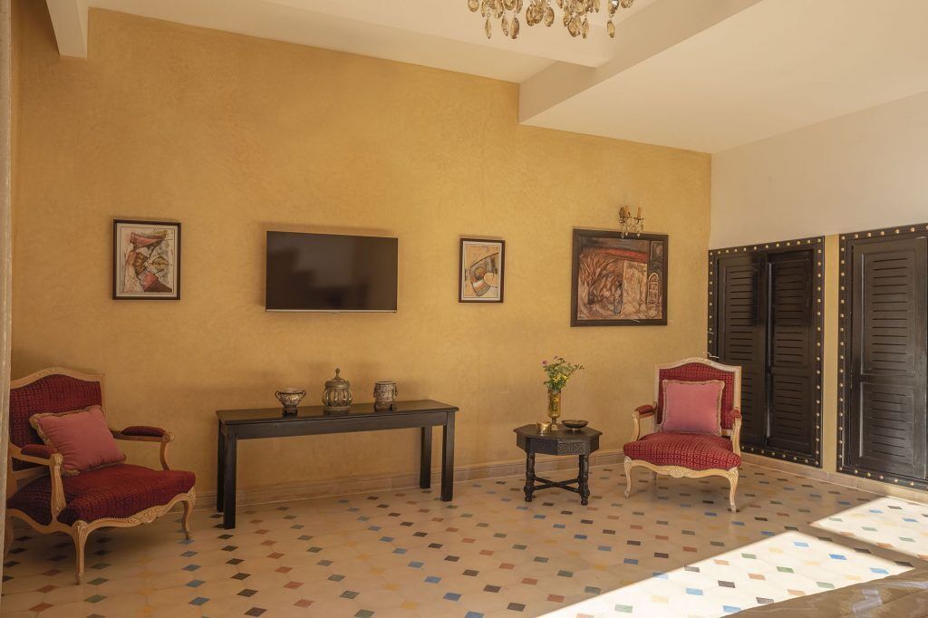 Una habitación con un televisor de pantalla plana grande, dos obras de arte enmarcadas, una mesita con objetos decorativos y dos sillones tapizados en rojo.