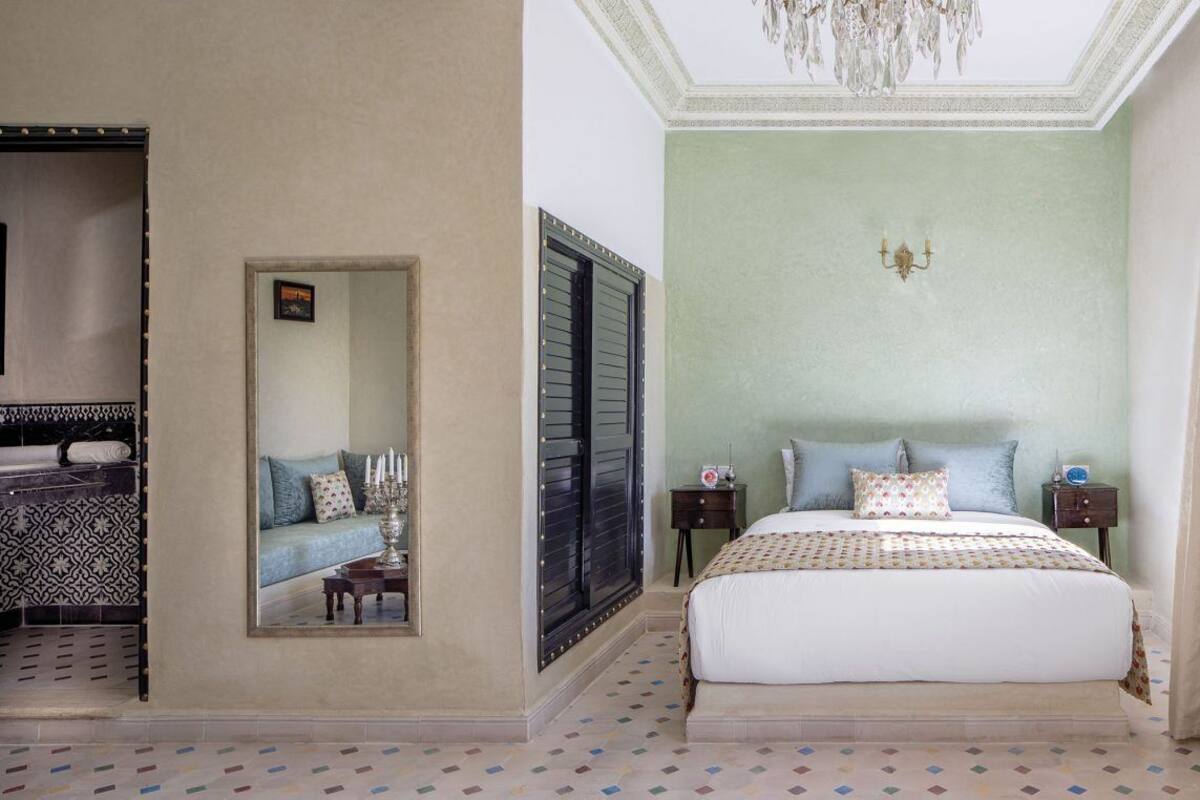 A bedroom with a bed, a nightstand, a mirror, a chandelier, and a patterned floor.