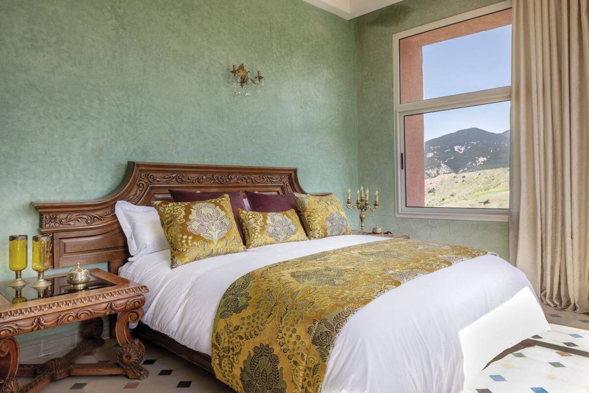 A bedroom with a large bed, a nightstand, a lamp, and a window with a view of mountains.