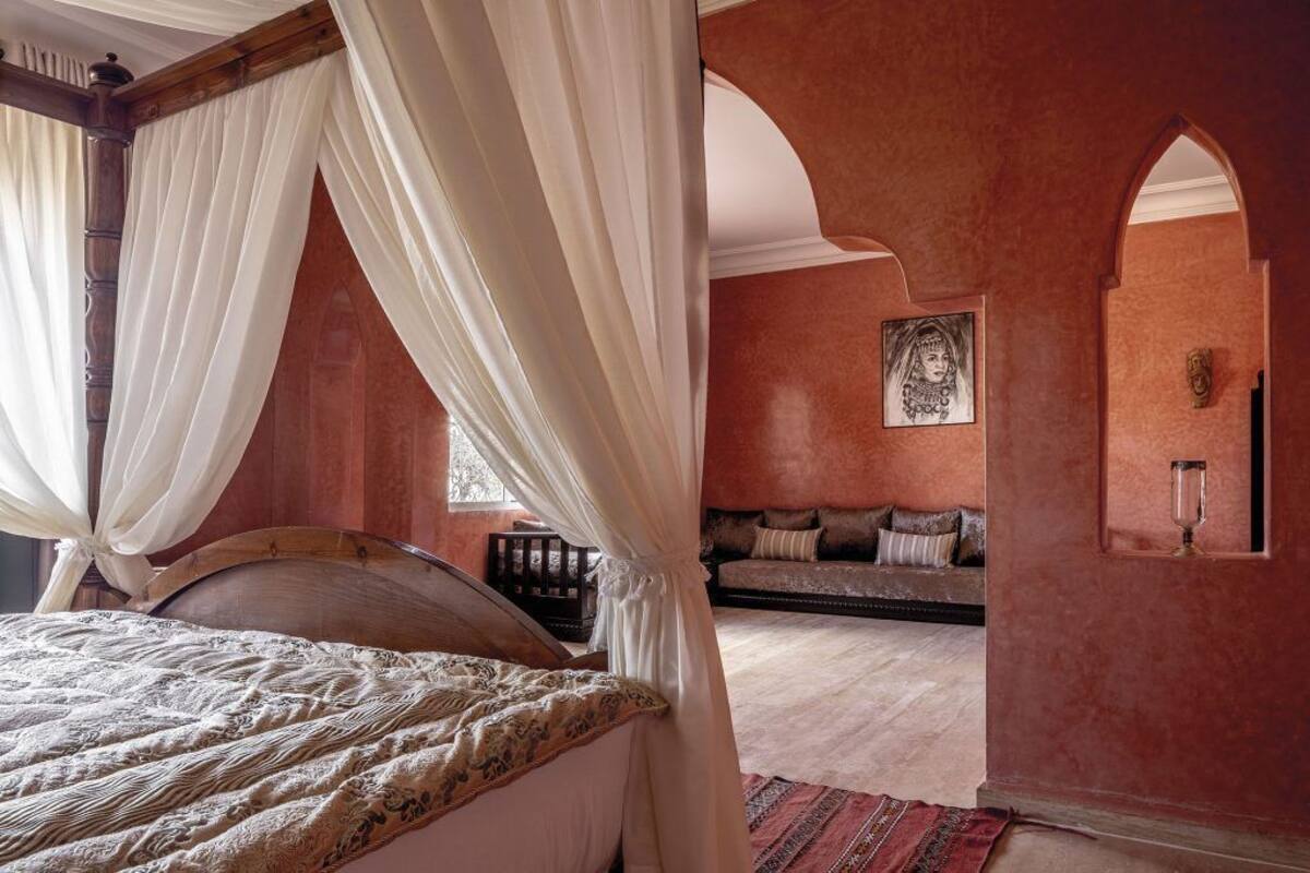 A bedroom with a four-poster bed, a sofa, and a decorative wall.
