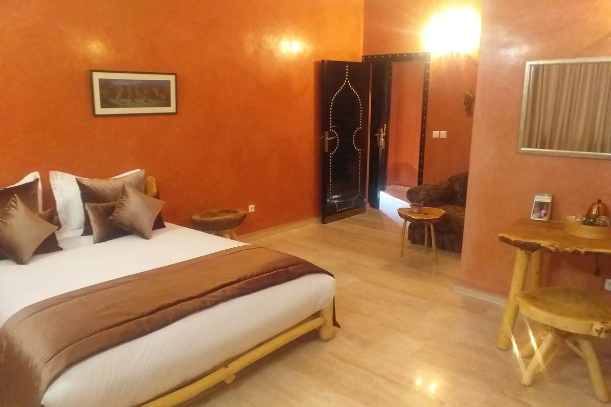 A hotel room with a bed, a small round table, a chair, and a wall-mounted shelf.