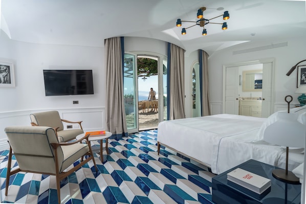 A hotel room with a bed, a chair, a TV, a table, and a view of the outdoors. - Borgo Santandrea (Amalfi)