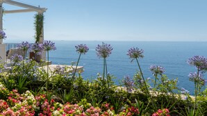 Een terras aan de kust met een pergola, bloemen en uitzicht op zee.