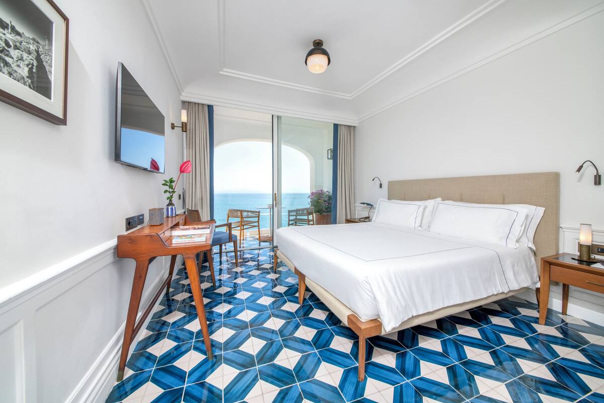 Een hotelkamer met een groot bed, een bureau met stoel, een televisie en uitzicht op zee.