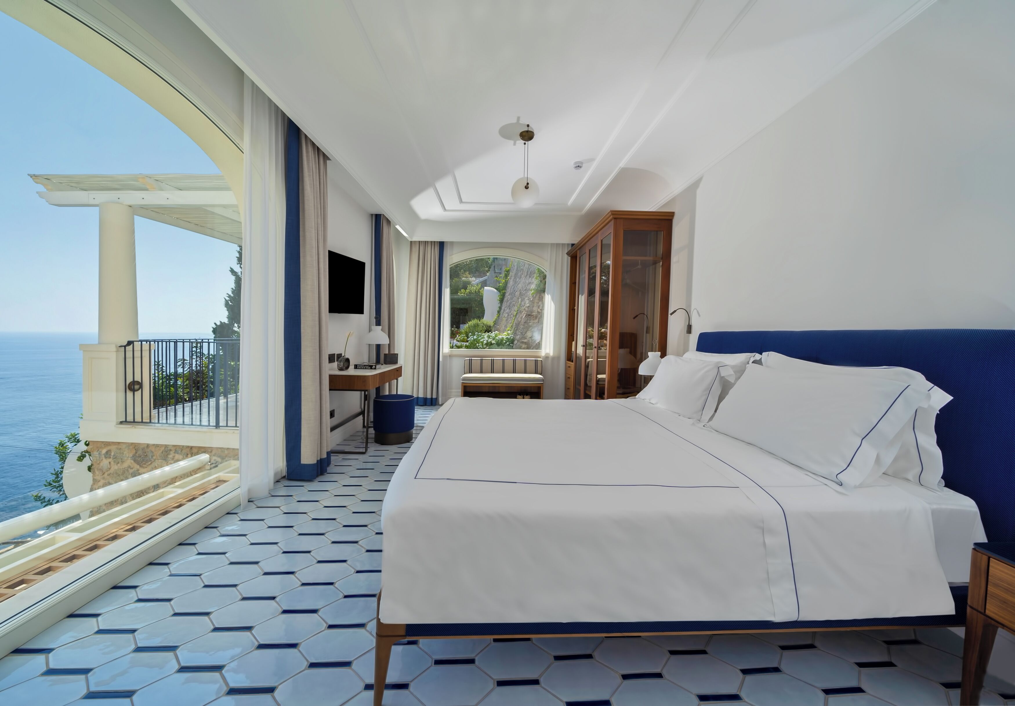 Ein Schlafzimmer mit großem Bett, Meerblick und einem Balkon mit Fliesenboden.