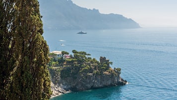 A coastal landscape with a rocky outcrop, clear blue sea, and distant mountains.