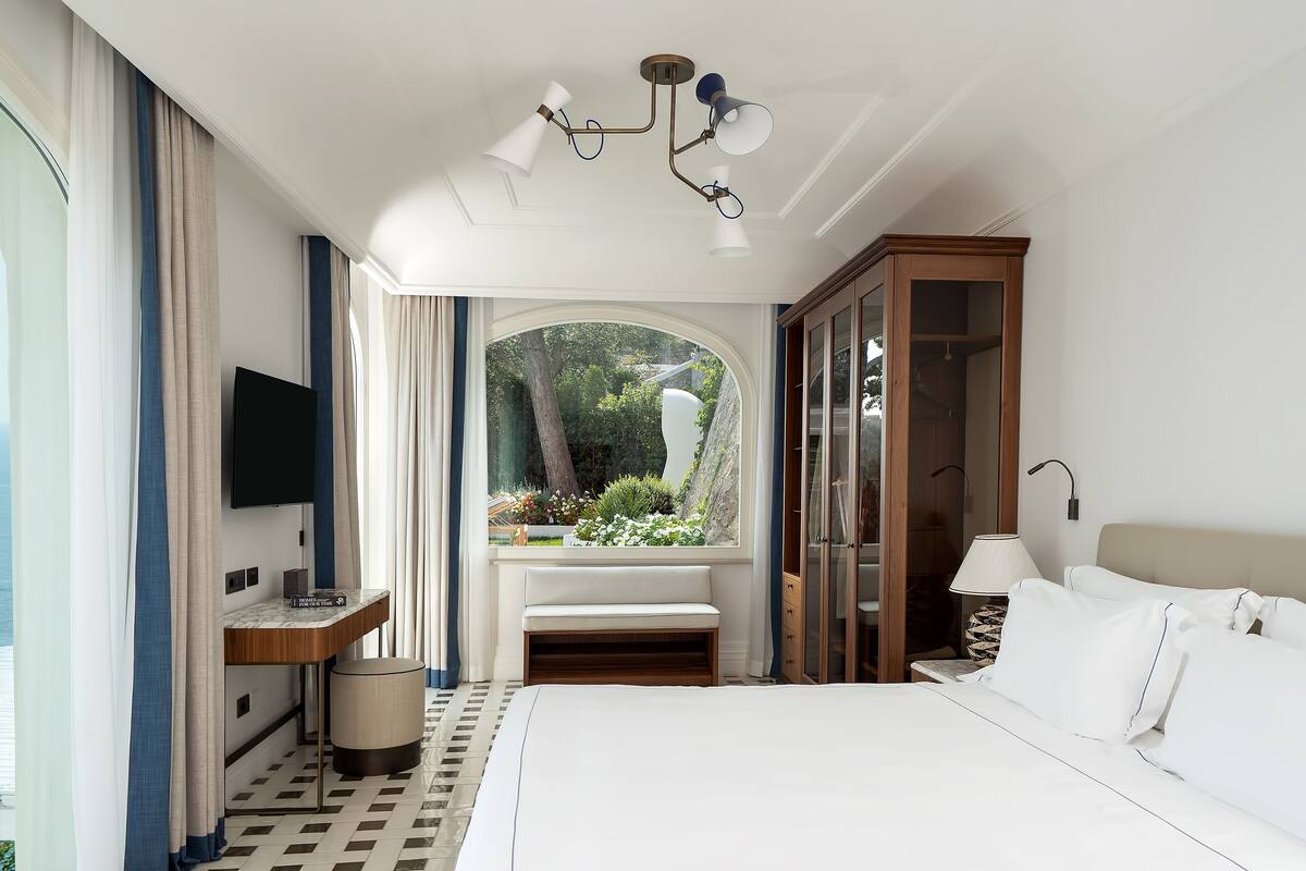 Een hotelkamer met een bed, een televisie, een bureau en uitzicht op zee.