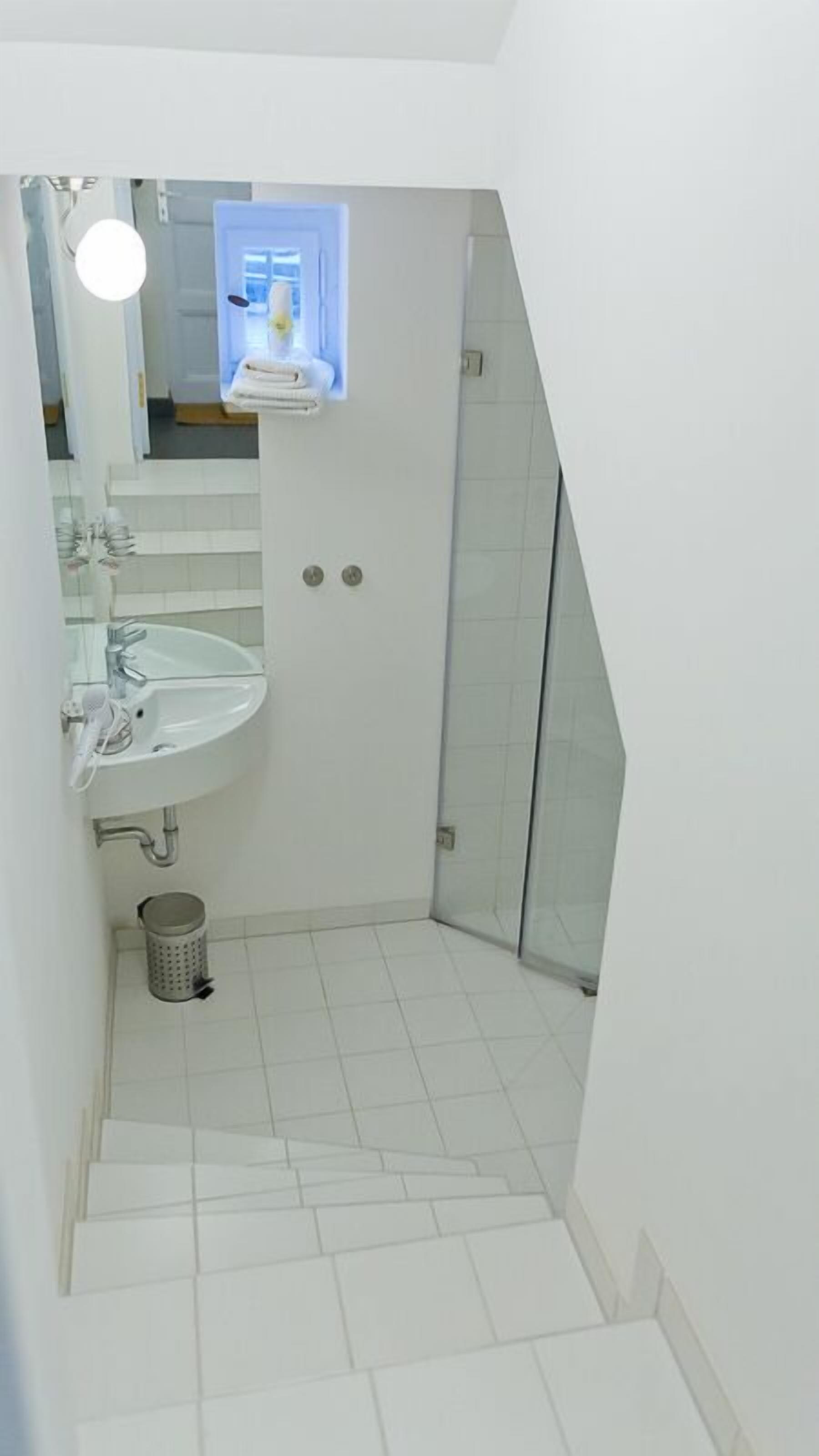 Un baño pequeño y blanco con lavamanos, espejo y ducha.